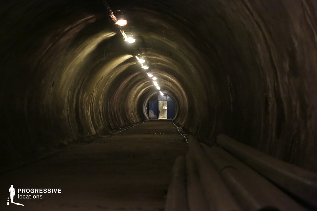 Narrow tunnel with stacked pipes and low lights, available as a film and photography location with industrial tone.