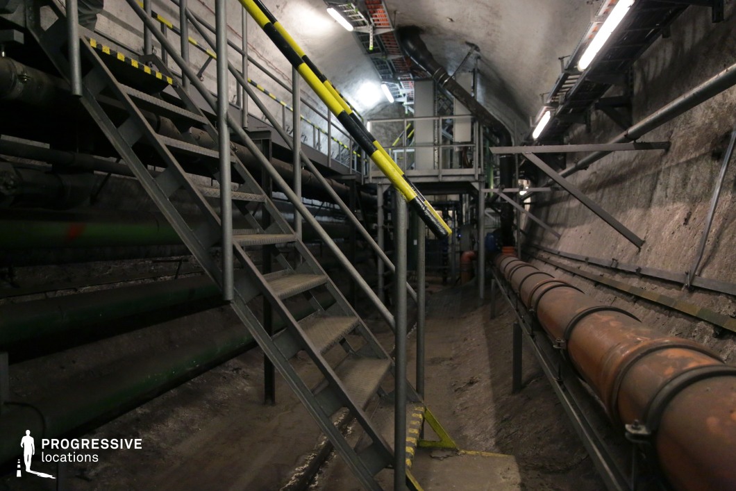 Industrial tunnel with steel stairs and pipes, used as a film and photography location for infrastructure scenes.