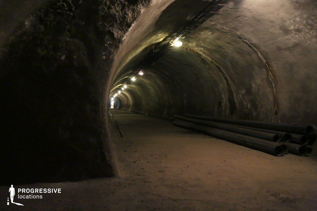 A dim concrete corridor with pipes and warm lighting, ideal underground film and photography location.