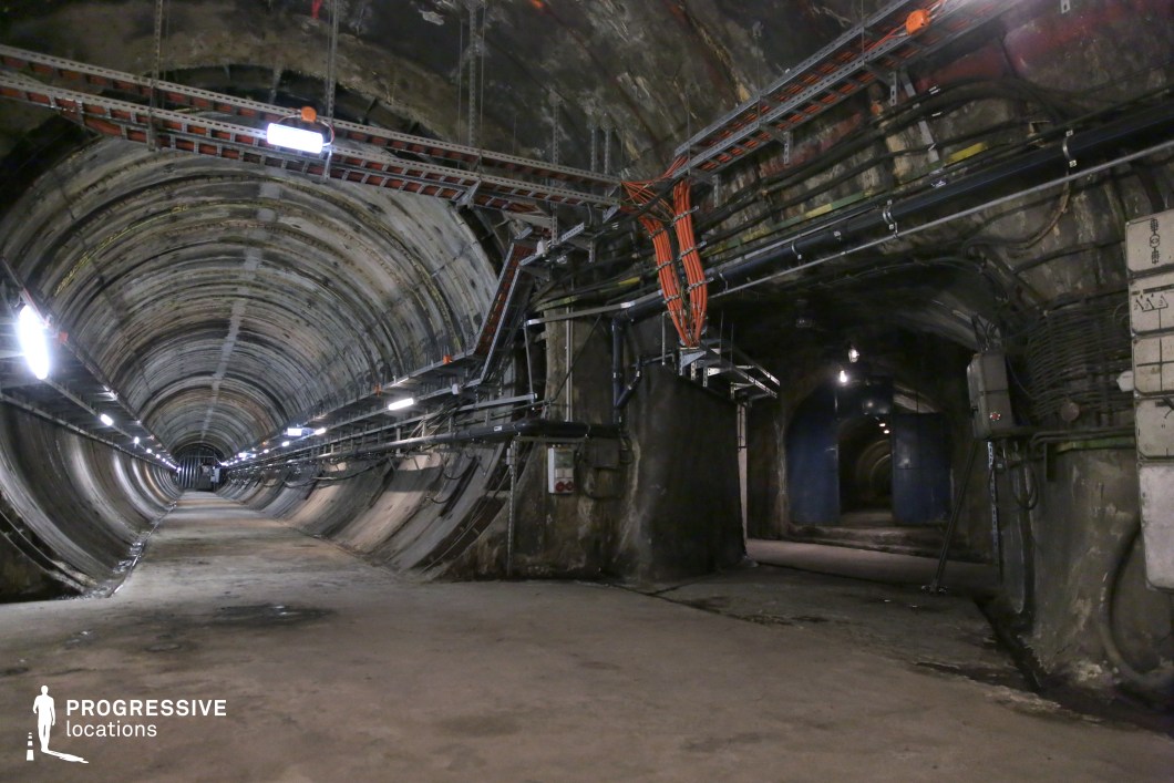 Concrete tunnel intersection with cables and lights, ideal film and photography location in an underground setting.