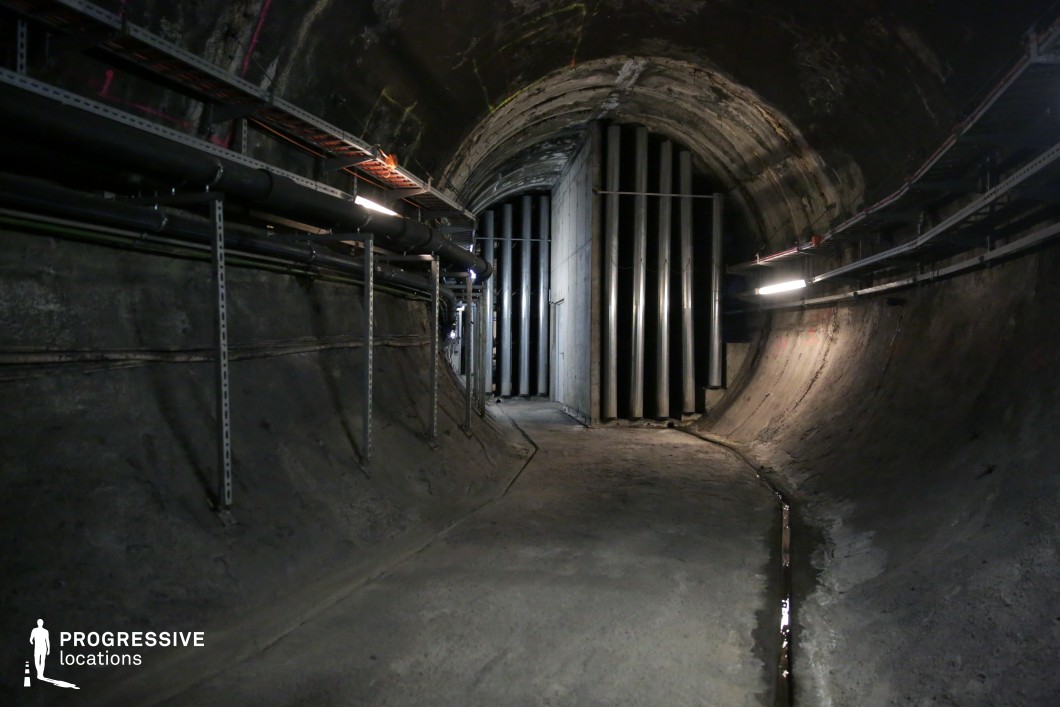 Underground tunnel with vertical pipes and steel fittings, a film and photography location with industrial realism.