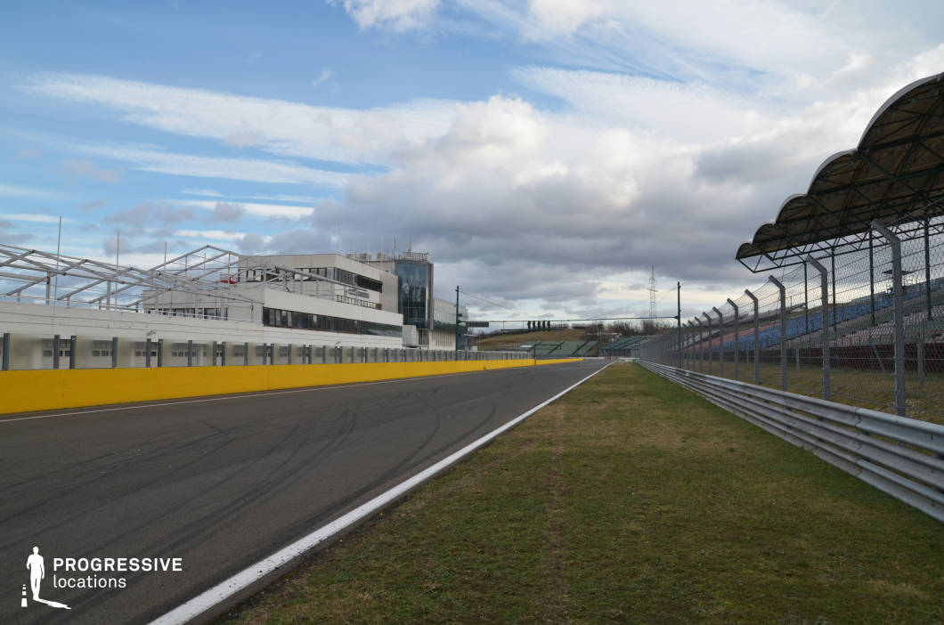 This wide, clean stretch of tarmac lined with safety barriers, fencing, and modern viewing stands belongs to a professional motorsport circuit, complete with control towers and timing structures. The orderly layout and functional architecture lend it an international and high-stakes atmosphere, ideal for capturing the energy of competitive racing. This location is perfect for action films, sports dramas, or commercials centered on speed, ambition, or endurance, particularly for scenes involving races, pit stops, or high-adrenaline chases.
