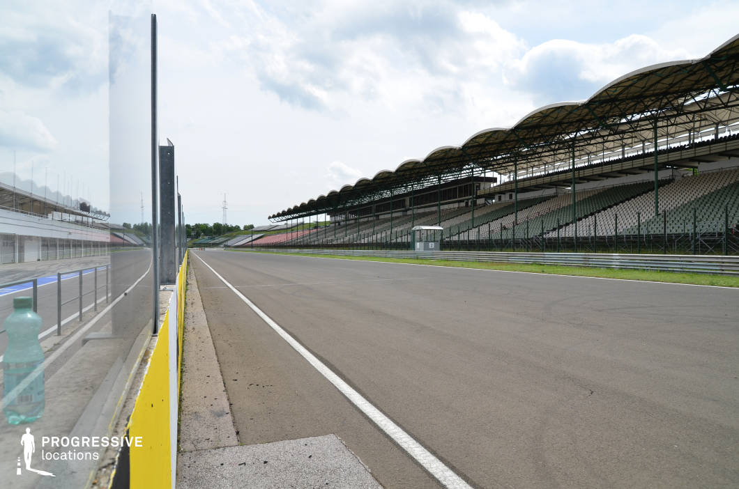 This location showcases a wide, straight section of a professional racetrack flanked by large, modern grandstands with distinctive arched canopies and tiered seating. The clean asphalt track, safety barriers, and expansive layout create a dynamic and high-energy visual environment. Its scale and architectural clarity make it ideal for filming high-speed action sequences, motorsport-themed scenes, or commercial shoots requiring a sleek, industrial backdrop. This setting works especially well for sports dramas, racing films, and adrenaline-driven commercials.