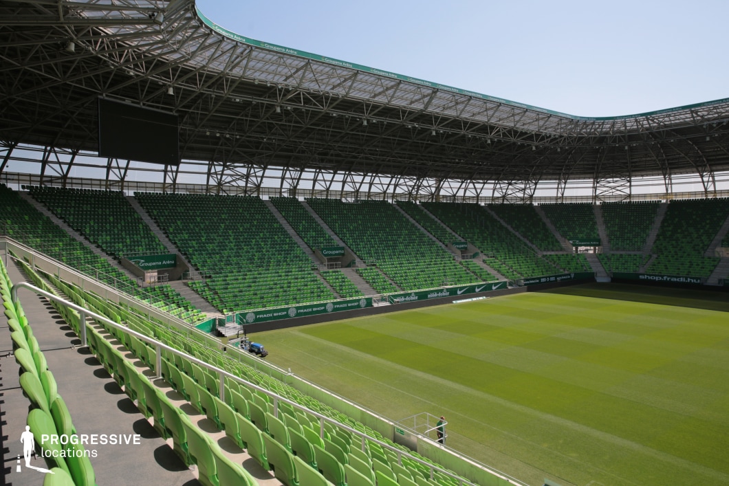 This image showcases a contemporary football stadium defined by its striking sea of green seats arranged in a steep, symmetrical configuration. The venue is enclosed with a partially transparent roof structure supported by an intricate steel framework, allowing natural light to penetrate while maintaining a sheltered atmosphere. The pitch is impeccably maintained, exhibiting a lush, uniformly mowed surface ideal for both close-up and wide-angle filming. The spatial layout ensures expansive views and unobstructed camera movement, with strong lines and repeated elements contributing to a dynamic visual rhythm. This location is especially suited for large-scale sports scenes, dynamic crowd simulations, or commercial productions requiring a bold, energetic backdrop.