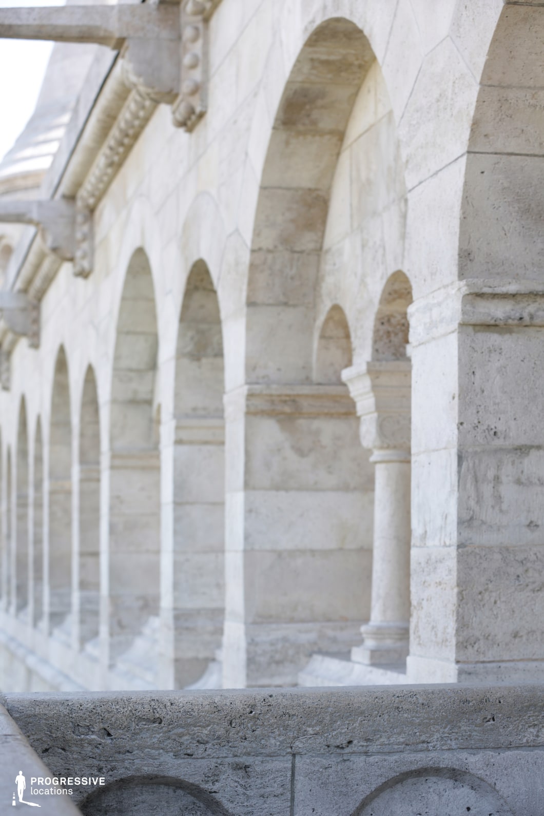 The image depicts a grand stone balcony, defined by a series of classical arches supported by sturdy columns. The stone surface displays a soft, weathered texture, adding character and age to the structure. The perspective emphasizes the depth of the arches, creating a sense of grandeur and openness. The symmetry and repetition of the arches, along with the columned support, suggest an architectural style that is both elegant and monumental. This location is ideal for filming historical, romantic, or dramatic scenes, particularly in settings that require a classical or regal backdrop. The visual appeal of the arches and columns provides a strong architectural feature, perfect for capturing expansive, formal settings in a variety of film genres, including period dramas, thrillers, or architectural showcases.