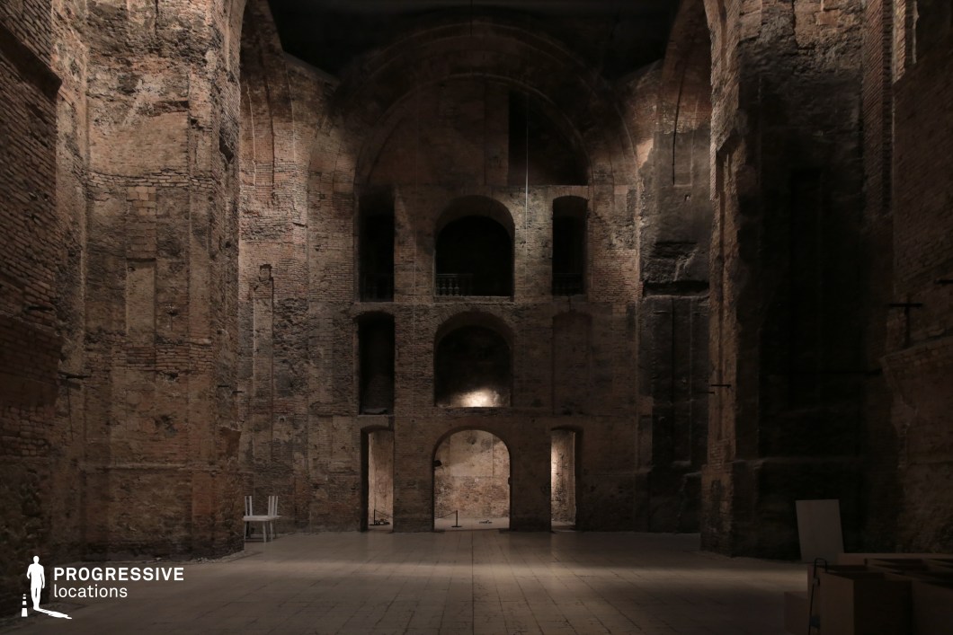 This image captures a cavernous, dimly lit interior with towering brick walls, high archways, and multiple recessed openings that add depth and mystery to the space. The aged, textured surfaces show signs of erosion and decay, reinforcing a historical or abandoned atmosphere. The central focal point is a series of arched openings stacked at different levels, adding a sense of grandeur and symmetry. The interplay of light and shadow enhances the dramatic quality of the setting. This location is highly suitable for filming historical dramas, fantasy epics, or psychological thrillers, serving as a medieval fortress hall, ancient temple ruins, or a mysterious underground chamber.