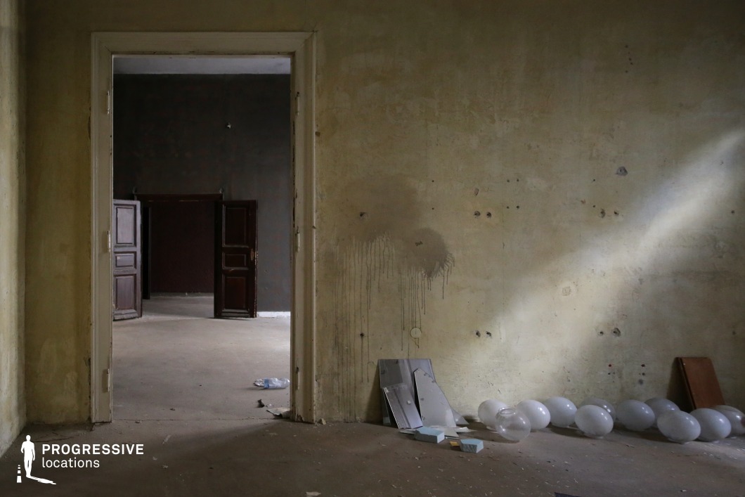 This deteriorating interior features cracked, stained walls and a floor covered in dust and scattered debris. The layered doorways create a strong visual depth, leading from a dimly lit foreground into progressively darker spaces beyond. The contrast between light and shadow enhances the eerie, desolate atmosphere. The pale yellow tones of the peeling walls contrast with the deep brown of the wooden doors, adding a sense of timeworn decay. This location is ideal for filming psychological thrillers, horror films, or post-apocalyptic stories, offering a setting that evokes themes of isolation, mystery, and forgotten history.