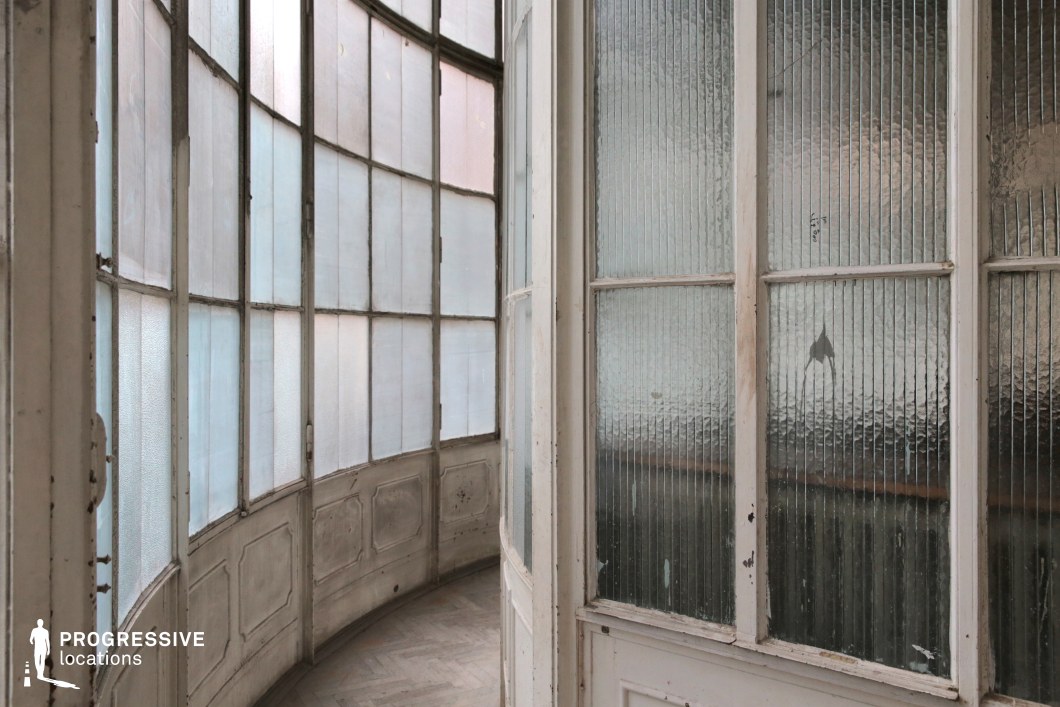 This curved glass corridor features a sequence of aged, frosted, and textured glass panels framed in white-painted wood, now worn with time. The soft diffusion of light through the semi-opaque windows creates a muted, atmospheric glow, while the curved architecture enhances the sense of movement and depth. The slightly distressed surfaces, including chipped paint and a fractured pane, add a touch of nostalgia and mystery. The minimalist color palette of pale whites and soft grays contributes to a dreamlike, timeless aesthetic. This location is ideal for filming psychological dramas, art-house films, or period pieces, offering a visually striking backdrop with an air of faded elegance and quiet intrigue.
