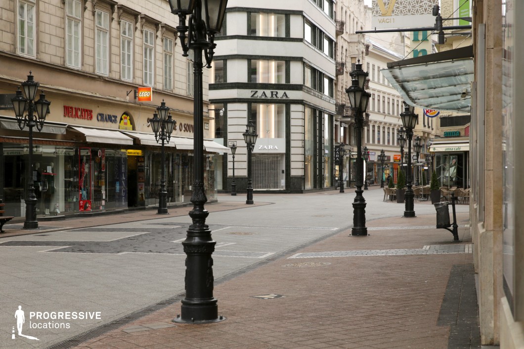 This image showcases a refined European shopping street, blending classical and modern architecture. The pedestrian walkway is lined with historic buildings featuring decorative facades, large shop windows, and a mix of upscale retail stores and smaller boutique shops. Ornate black lampposts punctuate the paved street, adding to the sophisticated atmosphere. The architectural contrast between the sleek white modern corner building and the traditional stone-clad structures enhances the visual appeal. This location is ideal for fashion shoots, romantic dramas, or high-end commercial productions, providing a stylish and atmospheric backdrop reminiscent of European luxury districts.