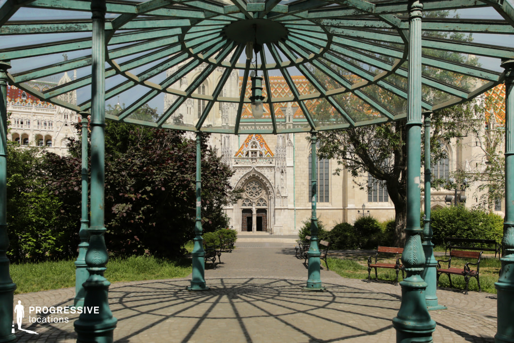Decorative iron gazebo with a view of a Gothic-style church facade, a film and photography location combining architecture and garden atmosphere.