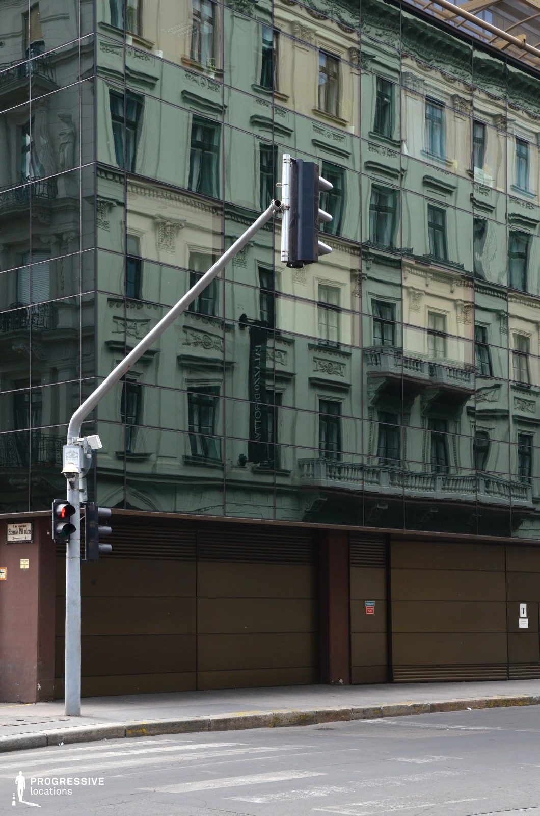 This urban scene juxtaposes modern and classical architecture through the distorted reflection of an ornate historic building on the sleek glass facade of a contemporary structure. The reflective panels create a fragmented and almost surreal visual effect, emphasizing contrast between past and present. A slightly tilted traffic light in the foreground adds an element of asymmetry, enhancing the urban dynamic. This location is ideal for films exploring themes of duality, perception, or modernization, making it a compelling backdrop for psychological thrillers, noir-inspired cinematography, or visually striking city montages.
