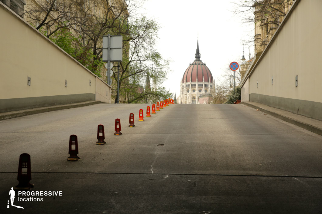 This urban incline leads toward a grand architectural landmark, framed by minimalist beige walls that create a tunnel-like perspective. The evenly spaced traffic dividers add depth and rhythm to the composition, guiding the eye toward the imposing domed building in the distance. The clean, structured aesthetic of the roadway contrasts with the ornate historic architecture beyond, making this location visually striking for cinematic reveals, suspenseful ascents, or establishing shots in dramas and thrillers.