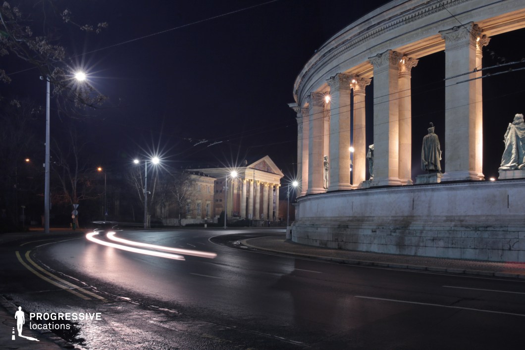  This grand neoclassical monument, featuring towering columns and statues, stands dramatically lit against the night sky. The curved road in the foreground reflects the glow of streetlights, with light trails adding a dynamic contrast to the structured, timeless architecture. In the background, another stately building with a triangular pediment enhances the classical atmosphere, reinforcing the location’s historical significance. The mix of artificial lighting, deep shadows, and monumental scale makes this an ideal setting for mystery films, historical dramas, or high-stakes urban thrillers, offering a cinematic balance of elegance and intrigue.