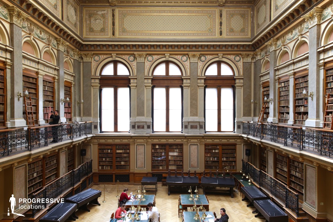 This magnificent two-story library exudes classical elegance with its soaring arched windows, intricate ceiling moldings, and elaborately decorated columns. The upper level features a wrought-iron balcony encircling the room, lined with towering wooden bookshelves filled with antique volumes. Delicate gold and pastel frescoes adorn the upper walls, enhancing the refined aesthetic. The parquet flooring, deep green reading tables, and brass desk lamps add a timeless academic ambiance. This location is ideal for filming historical dramas, intellectual thrillers, or period pieces, providing a distinguished backdrop for scholarly discussions, secret meetings, or moments of discovery.