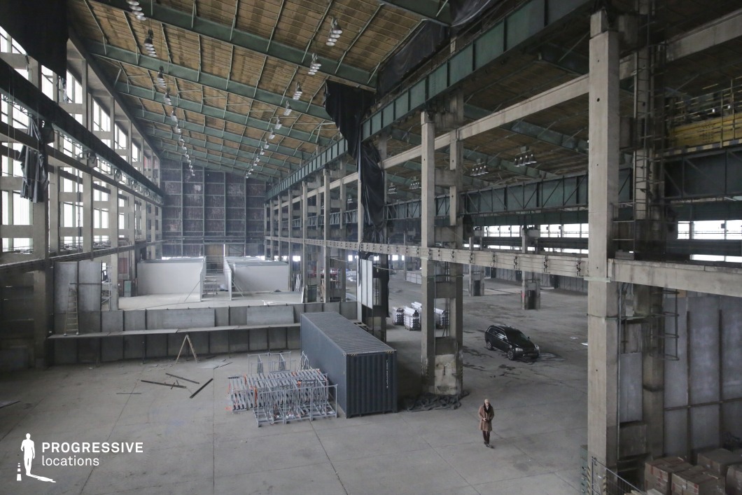 Vast industrial hangar interior with concrete columns and steel roof trusses, an ideal film and photography location for large-scale productions.
