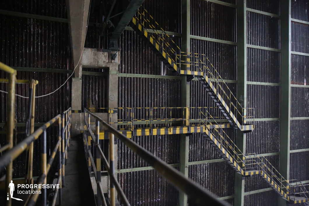 Multi-level industrial staircase and metal walkways forming a photography and film location within a large industrial hall structure.