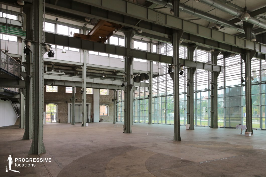 This expansive industrial hall combines historical and modern architectural elements, featuring steel framework, large arched brick windows, and contemporary floor-to-ceiling glass walls. The open floor plan, high ceilings, and exposed metal beams create a sense of vastness, while overhead lighting fixtures and ventilation ducts add an industrial aesthetic. Natural light floods the space through the transparent walls, offering a visually dynamic environment with reflections and depth. This versatile location is ideal for filming corporate dramas, fashion shoots, or futuristic urban settings, as well as transformation sequences in sci-fi or dystopian narratives.