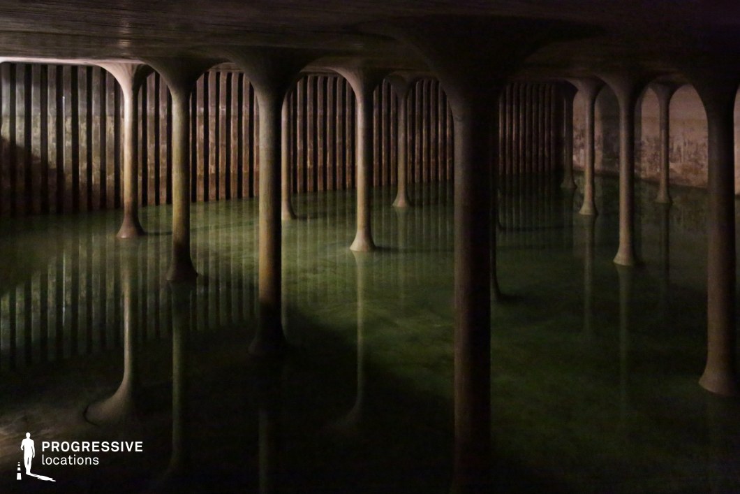 This eerie underground space features a vast array of smooth, rounded concrete columns rising from a still, reflective body of water. The dim lighting and rhythmic repetition of the pillars create an almost hypnotic sense of depth, while the darkened ceiling and ribbed perimeter walls add to the cavernous, industrial atmosphere. The greenish hue of the water enhances the mysterious, otherworldly quality of the setting. This location is ideal for filming suspenseful, dystopian, or sci-fi scenes, offering a unique, hauntingly beautiful backdrop for exploration, secrecy, or psychological tension.