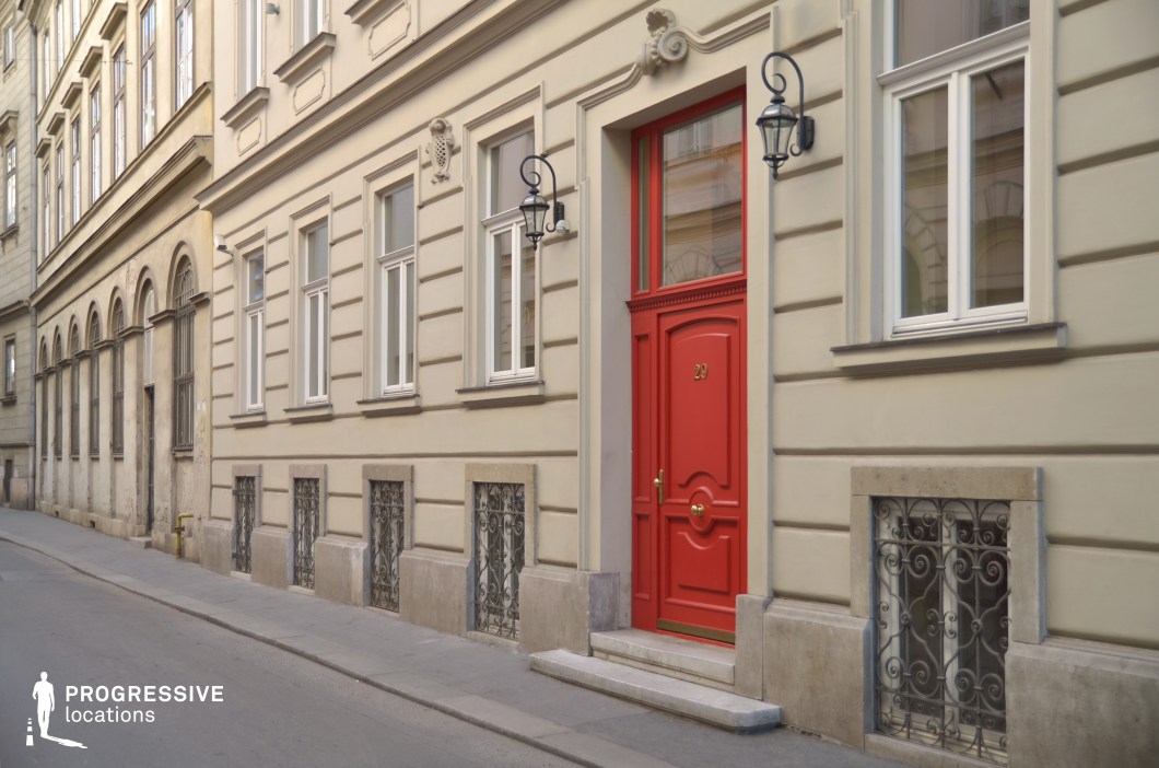 Light facade with red door and metal window grilles, ideal location for photography and filming with clean composition and strong color contrast