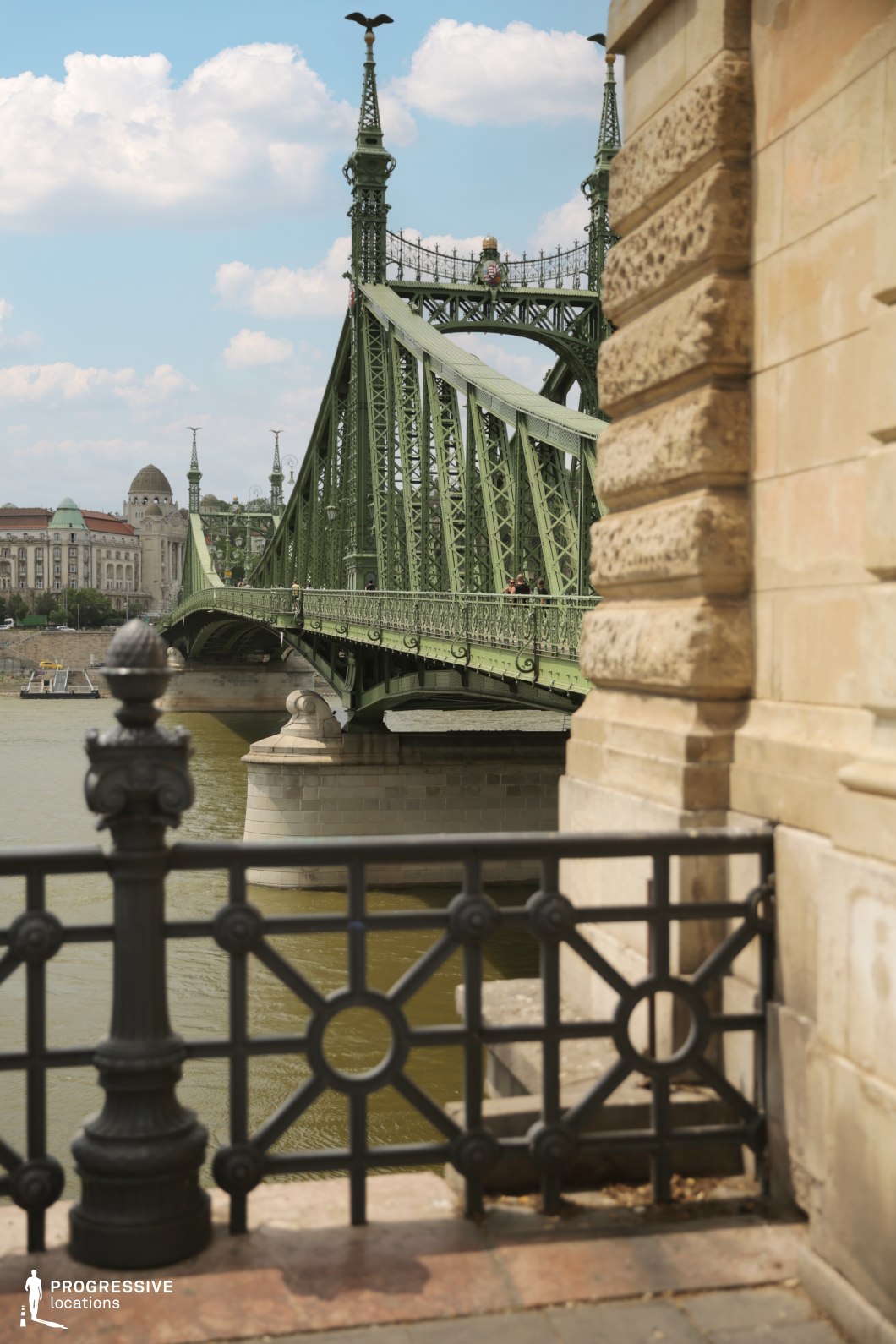 Historic green bridge spanning a river with surrounding buildings as an ideal location for photography and filming