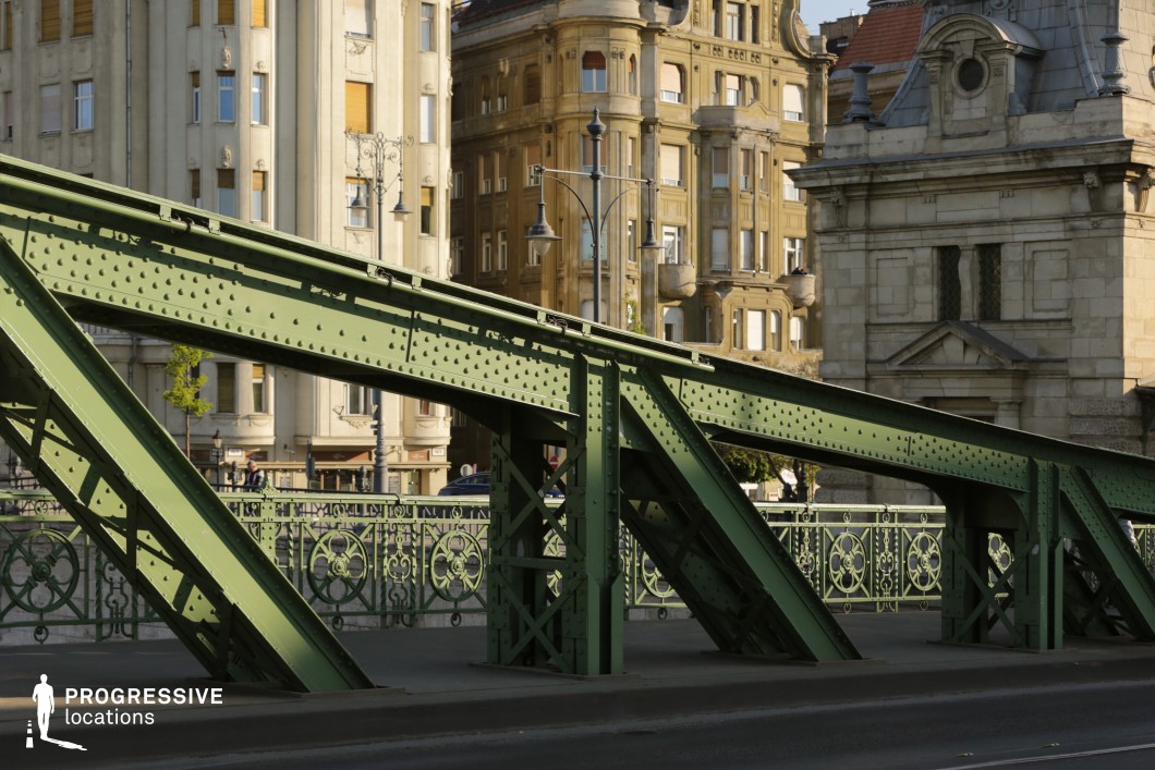 Green steel bridge truss crossing in front of historic buildings as a film and photography location