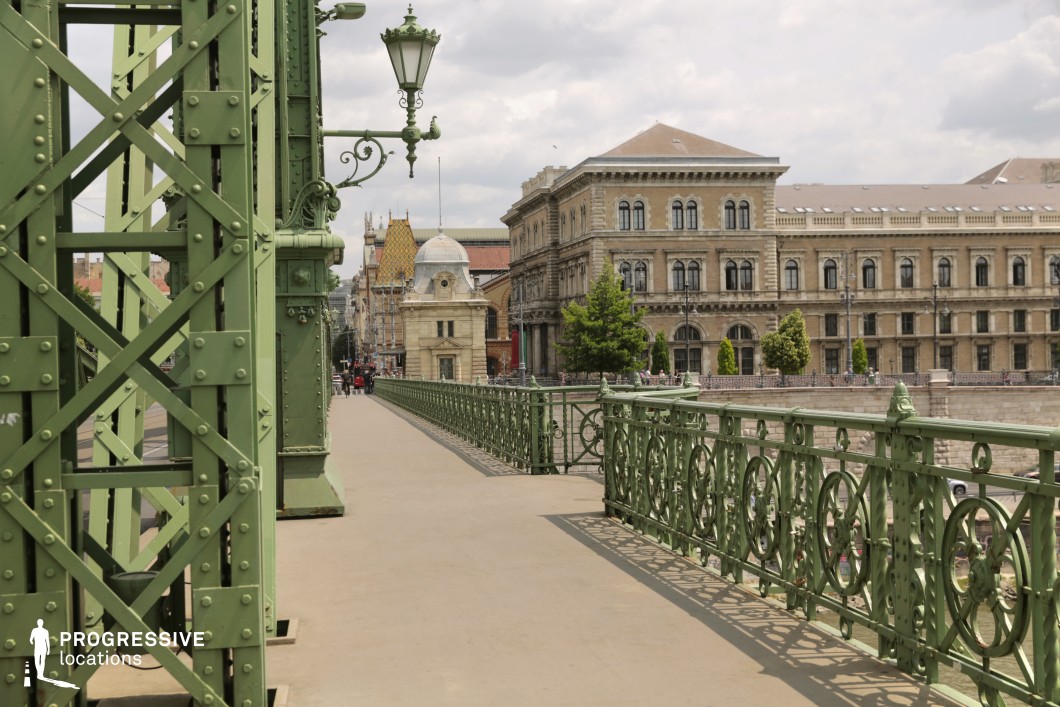 Bridge walkway with ornate green railing leading toward historic buildings as an ideal location for photography and filming