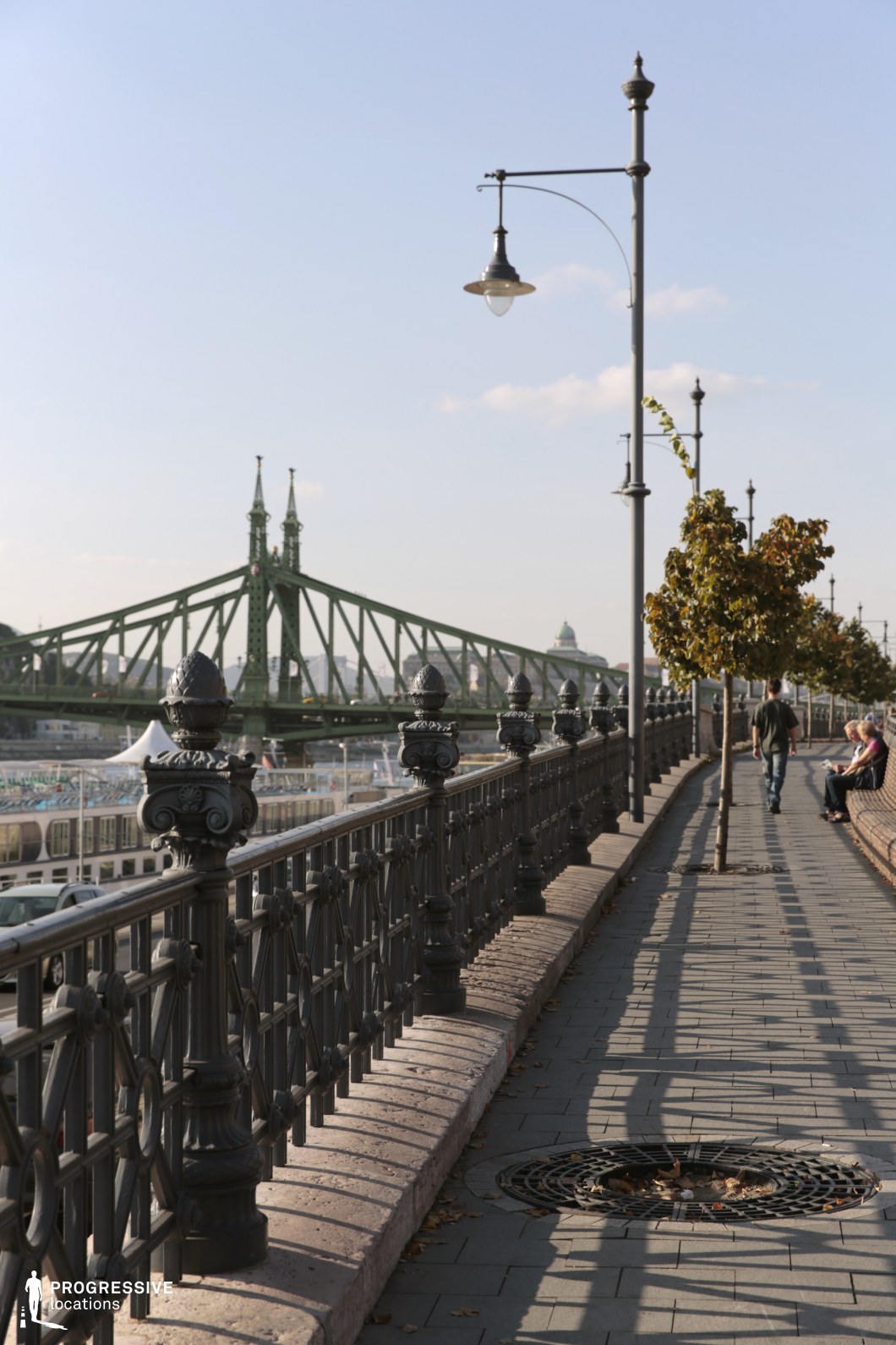 Riverside promenade with railing and lampposts leading toward bridge as a film and photography location