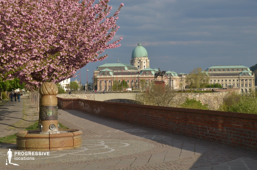 Riverside walkway with small fountain and palace view, photography and film location combining urban landscape and architectural backdrop