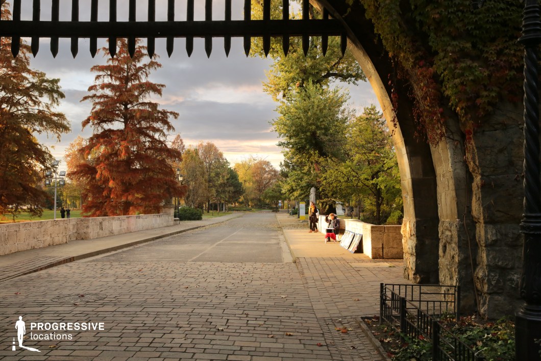 Stone archway opening to a paved street, ideal location for photography and filming with framed perspective and urban pathway