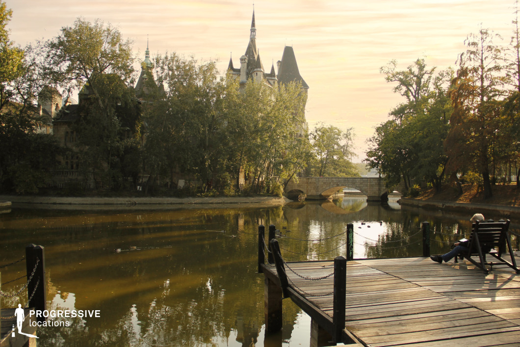 Lakeside view with stone bridge and castle buildings, film and photography location featuring water reflections and wooden pier