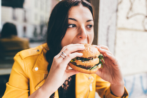 Young woman sitting in a restaurant eating an hamburger hand hold- hunger, food, meal concept