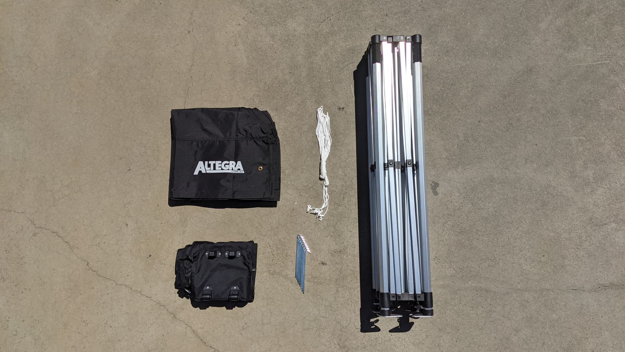 A lightweight aluminium gazebo frame in silver, with a black carry bag and accessories laid out on a surface.