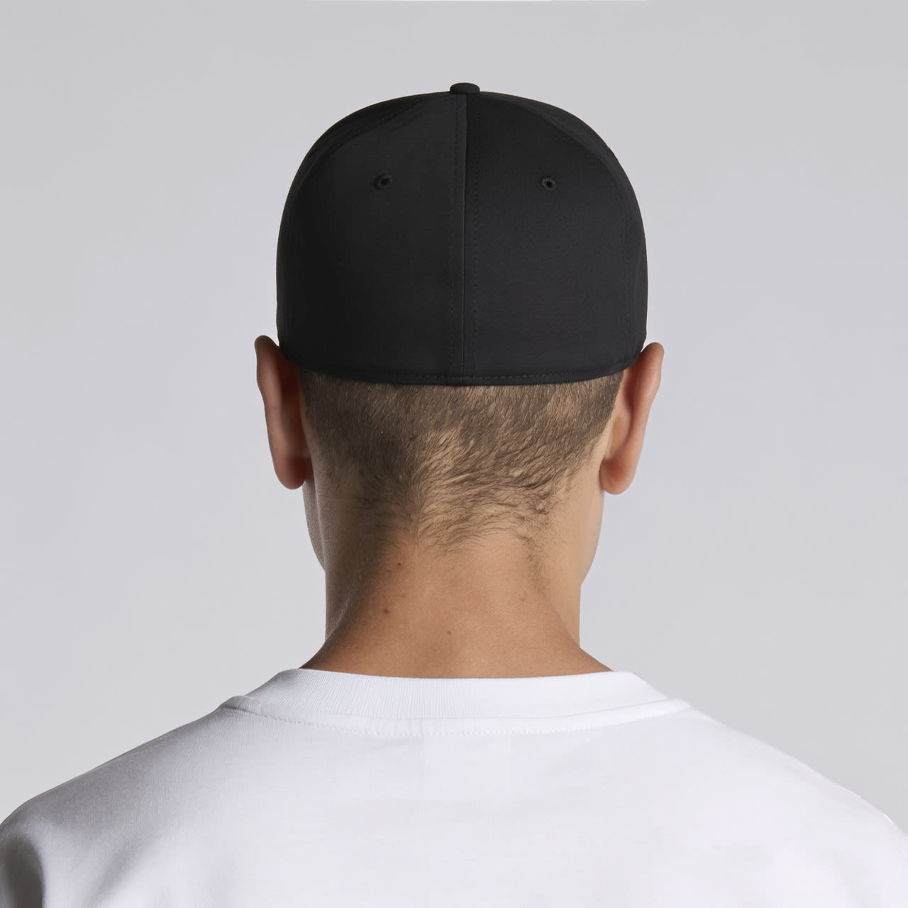 Stock Flex Cap AS-1106 A black cap is worn backwards by a person with short hair, featuring a logo on the back.