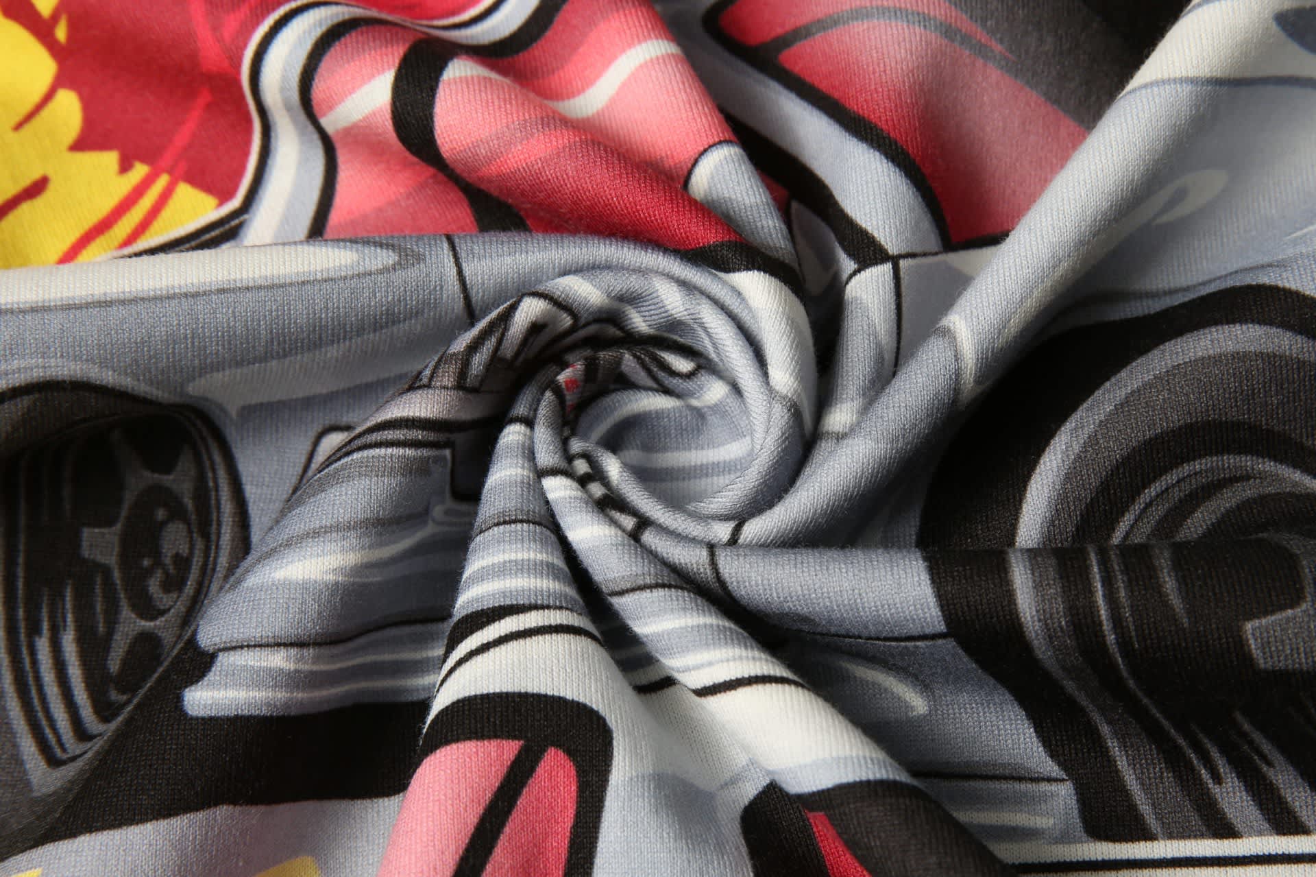 A spiral view of a fabric featuring a colourful print with red, yellow, and black designs on a light blue background.