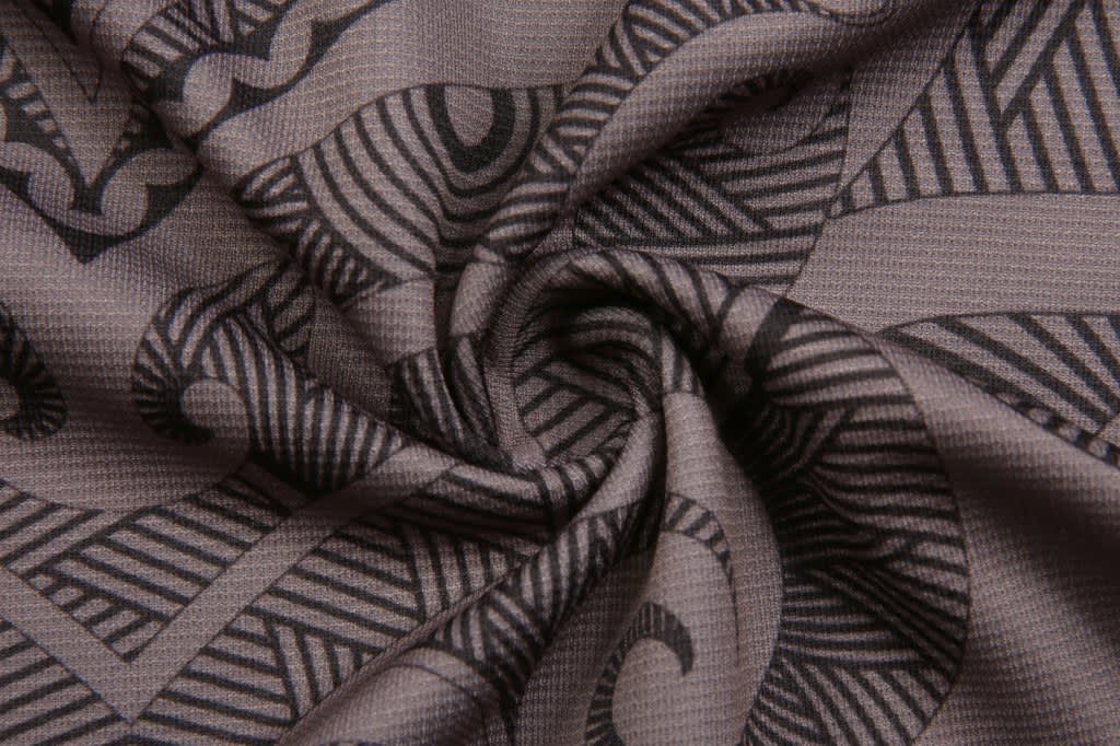 A close-up of a patterned fabric featuring intricate black designs on a grey background.