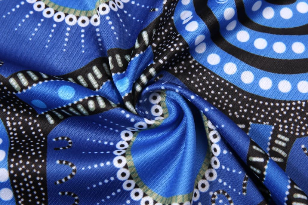 A patterned fabric featuring vibrant blue, black, and white designs, showcasing intricate motifs. The fabric has a smooth texture.