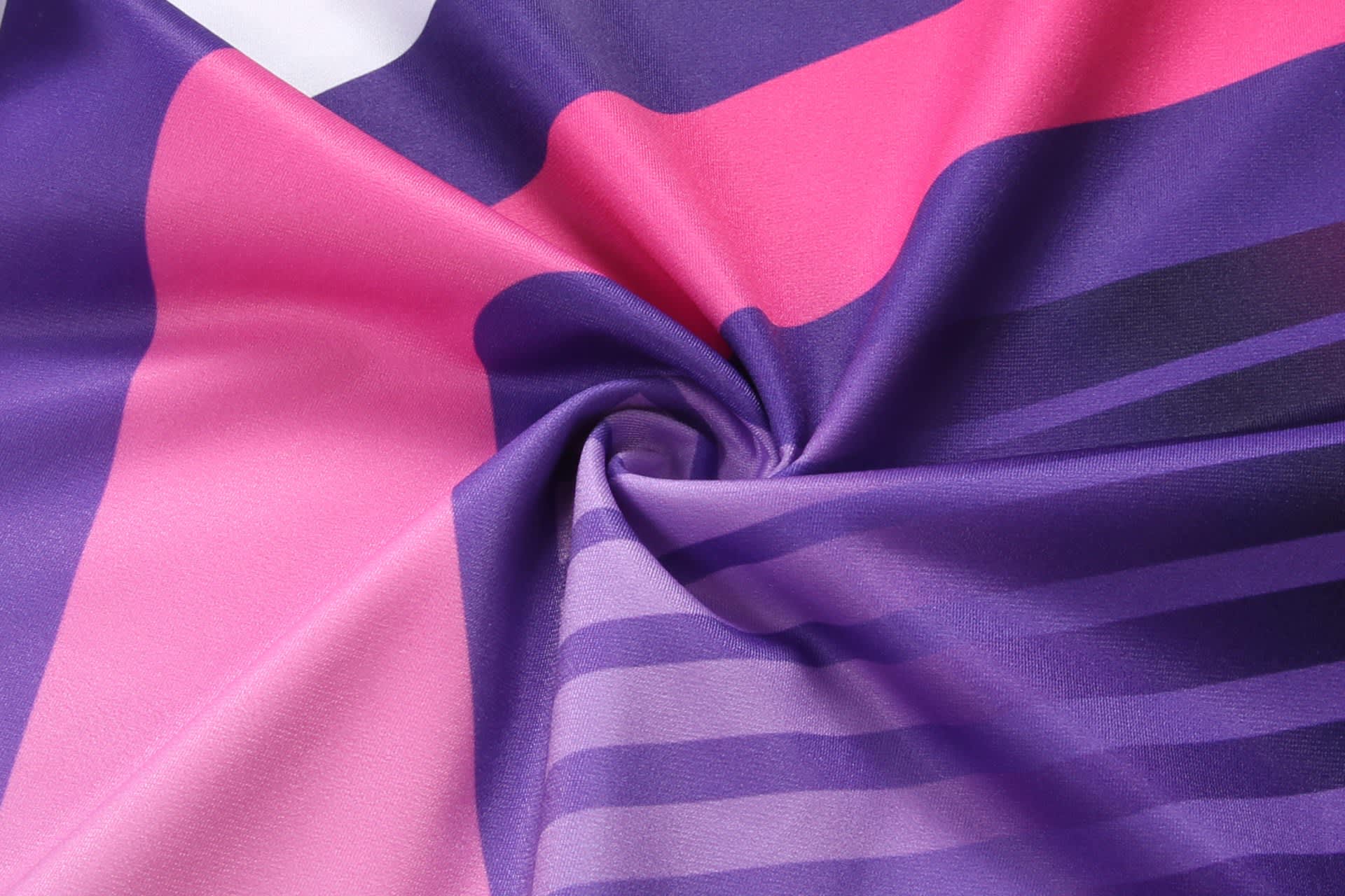 A vibrant fabric featuring a mix of purple, pink, and white patterns, showcasing a smooth, silky texture.