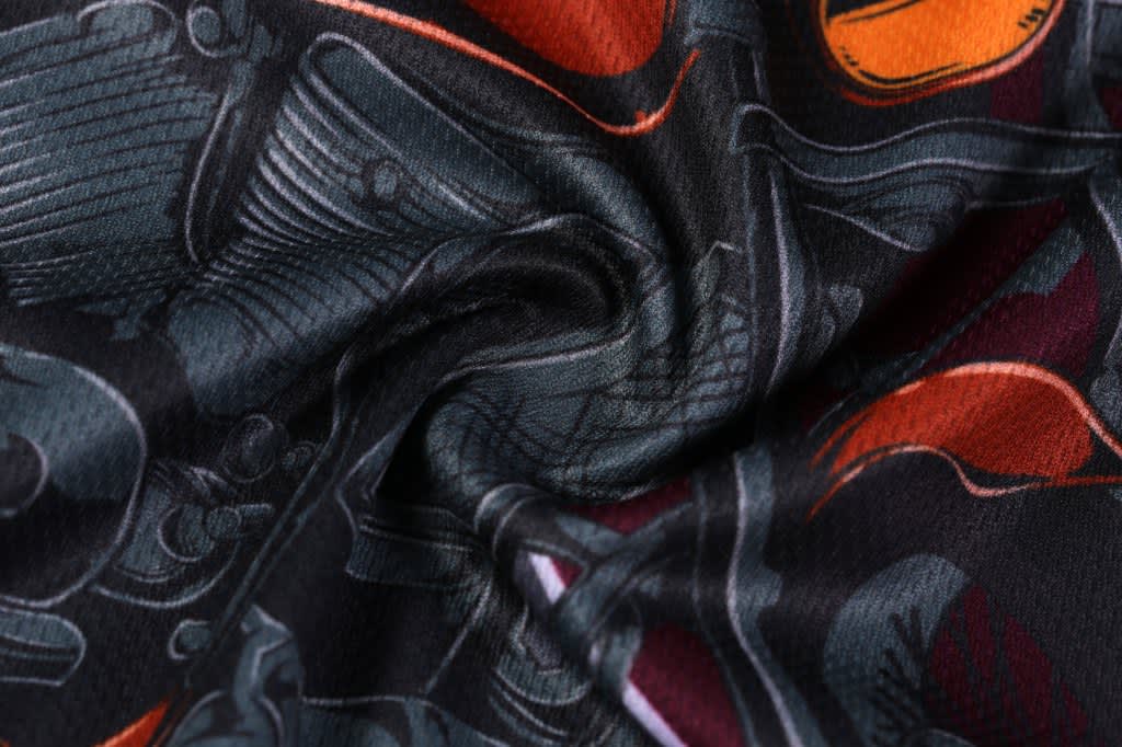 A close-up of custom motorcycle apparel featuring a black fabric with intricate designs of motorcycle parts in orange and grey.
