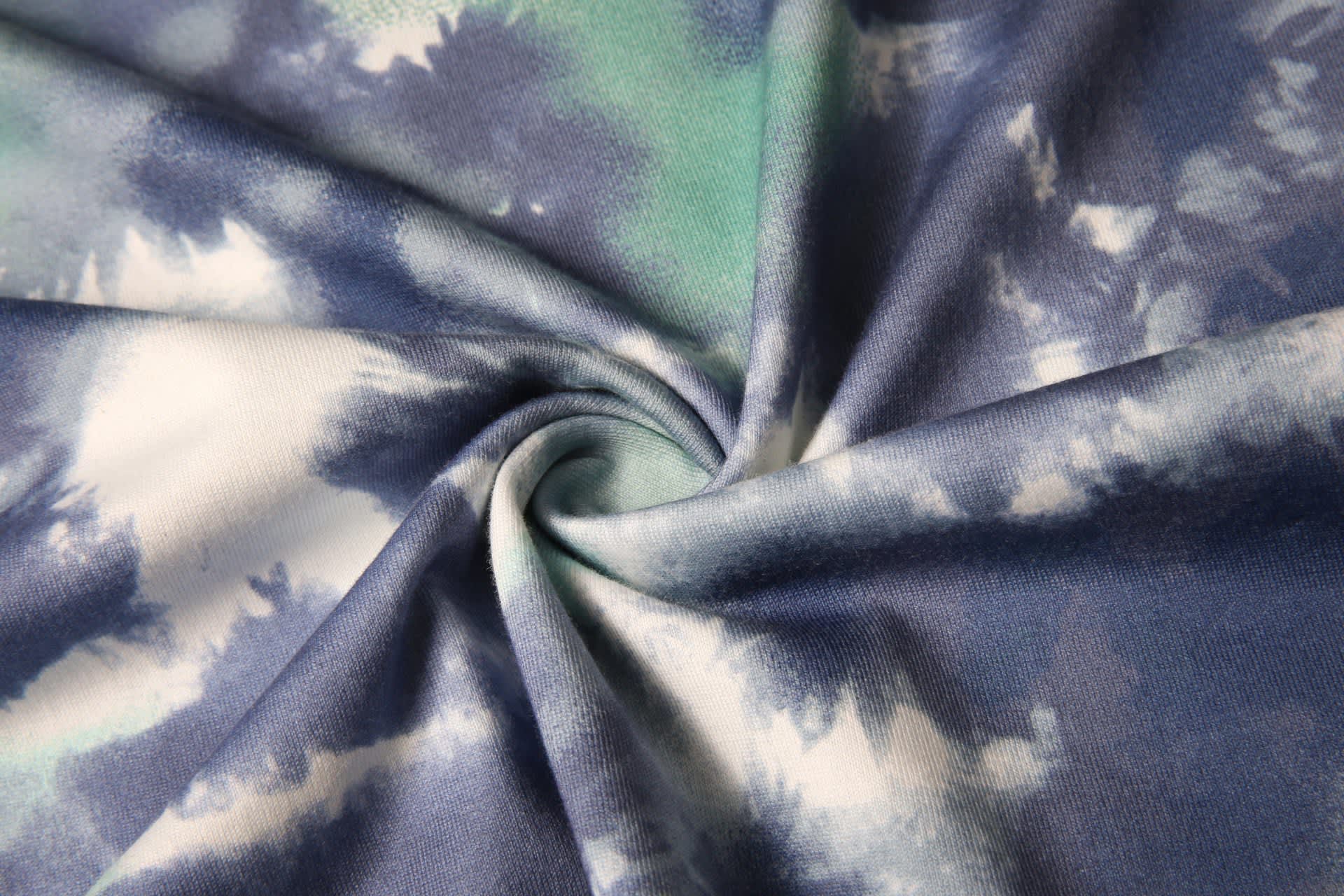 A swirling tie-dye fabric featuring shades of blue and green, showcasing a soft and textured surface.