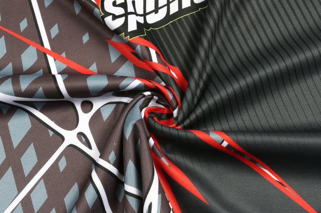 A close-up of fabric featuring grey, black, red, and blue patterns, with a logo visible.