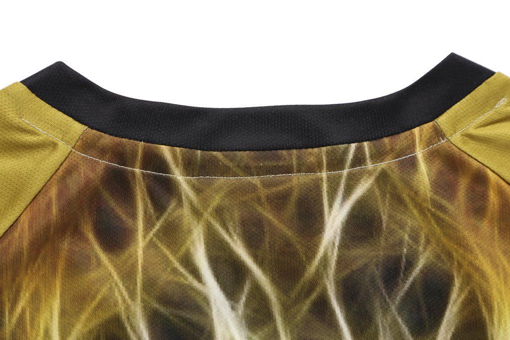 A sublimated T-shirt featuring a blend of earthy tones with a black collar and abstract patterns. It has a brand logo.