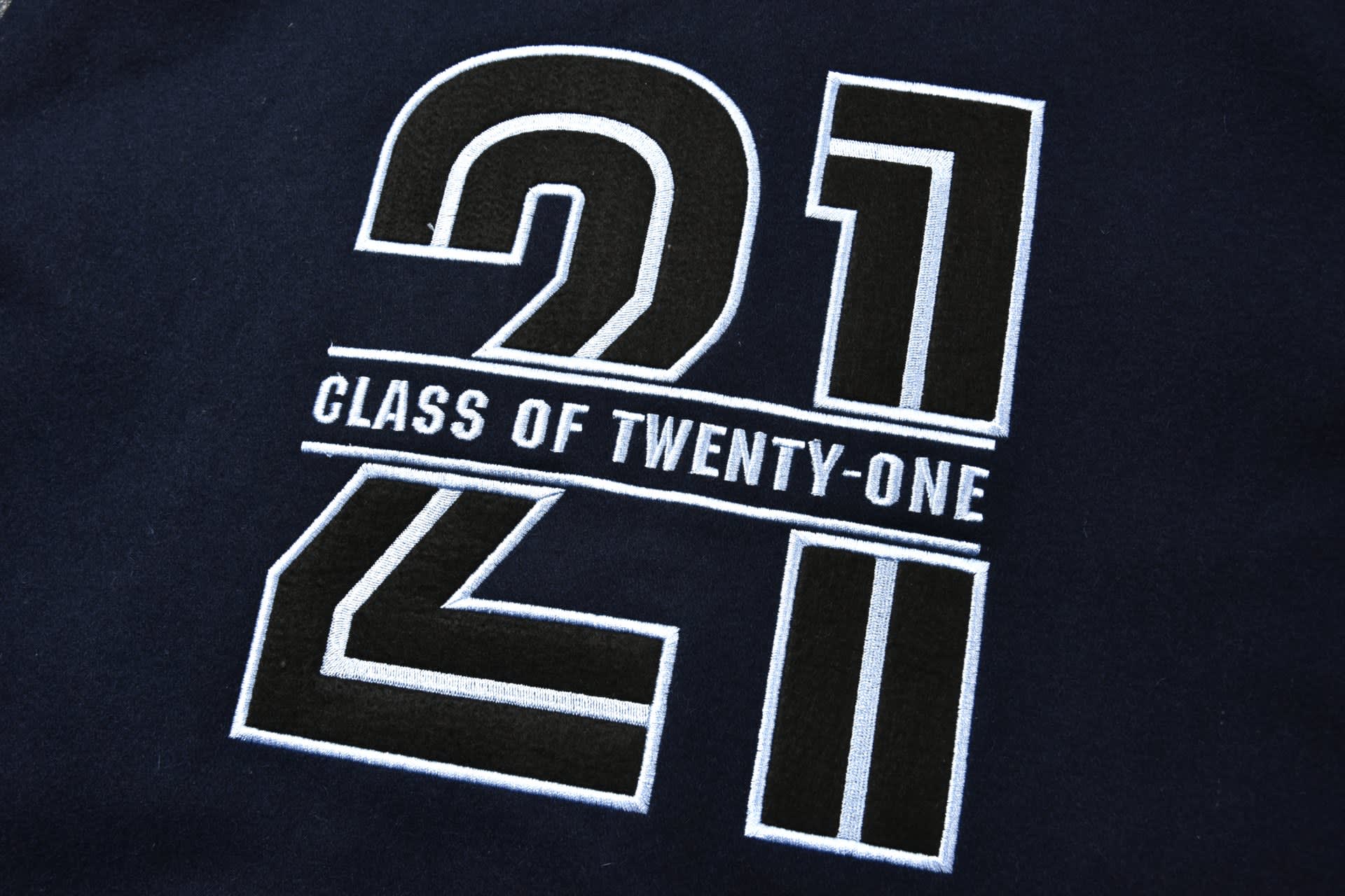 A dark fabric with embroidered numerals "21" and the words "CLASS OF TWENTY-ONE" in a bold design.