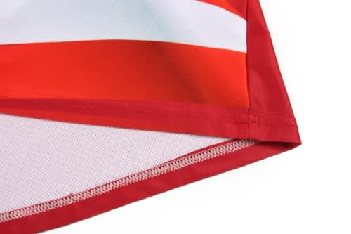 A close-up of a red and white striped soccer uniform, featuring mesh detailing and a logo on the fabric.