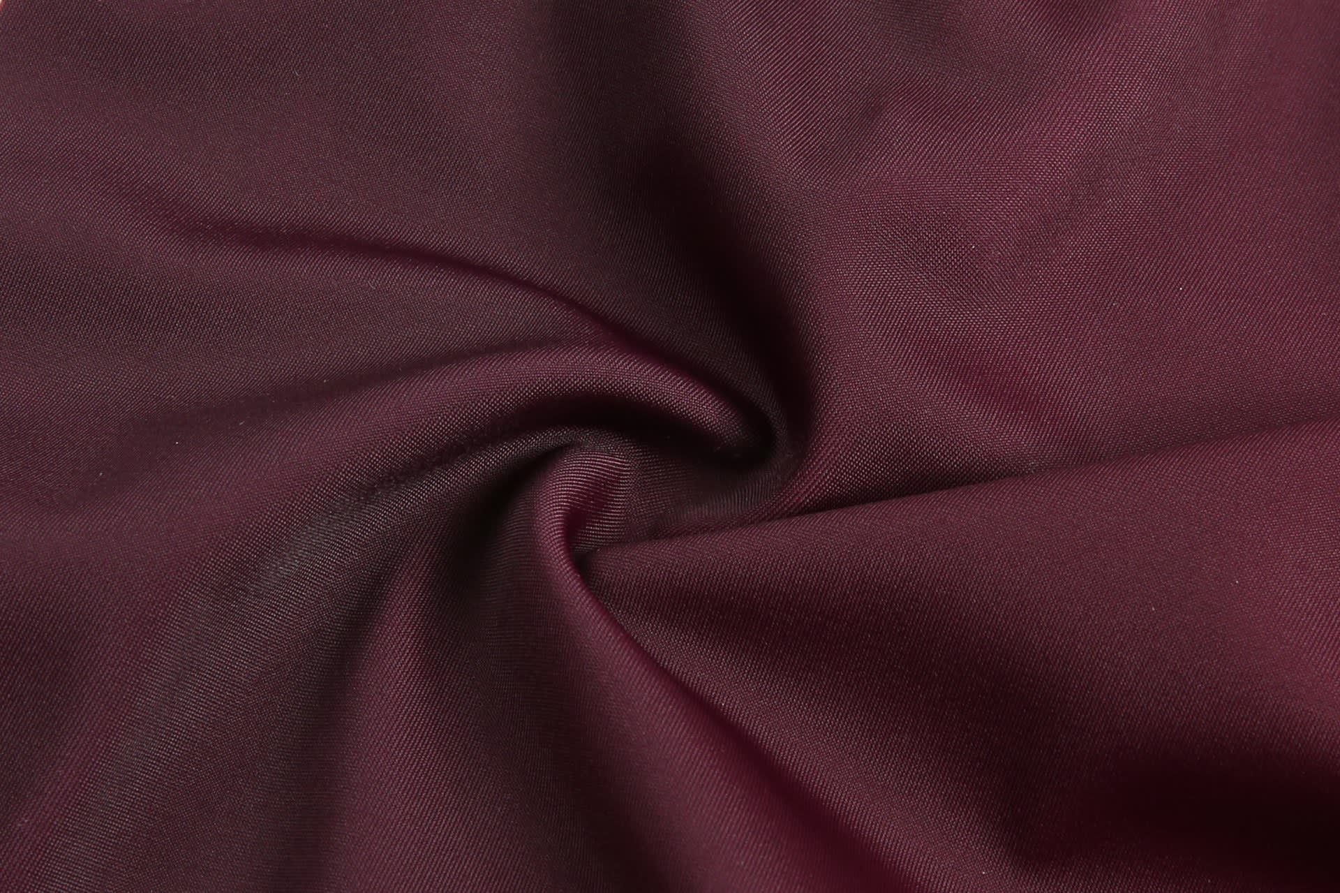 A maroon fabric swirled together, showcasing its smooth texture and vibrant colour, with a branding logo visible.