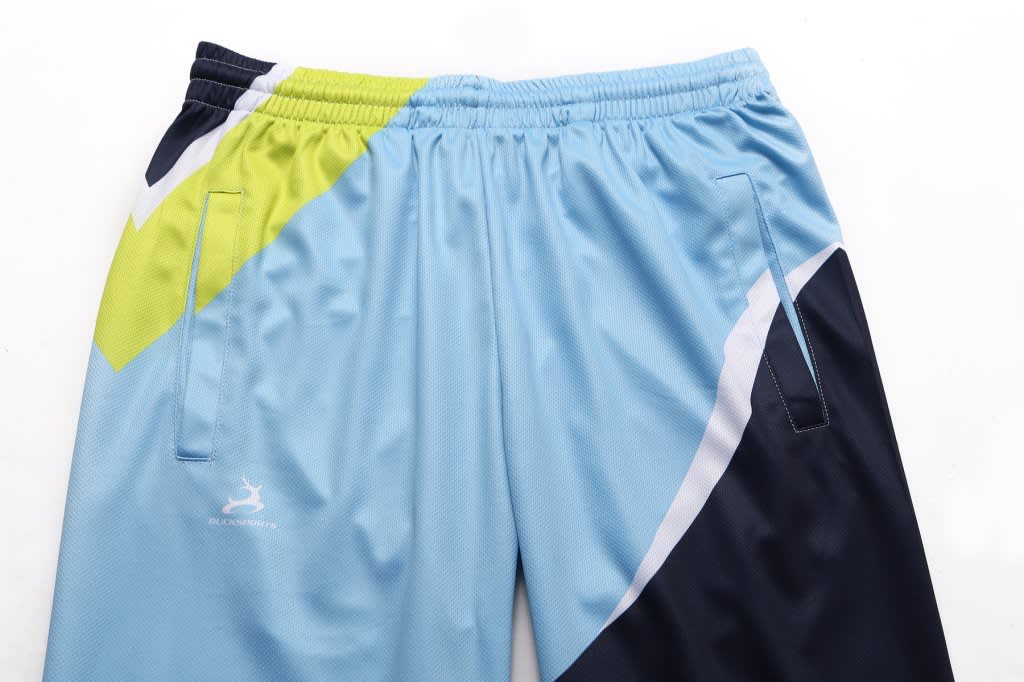 A pair of women's track pants in light blue, navy, and lime green, featuring side pockets and a branding logo.