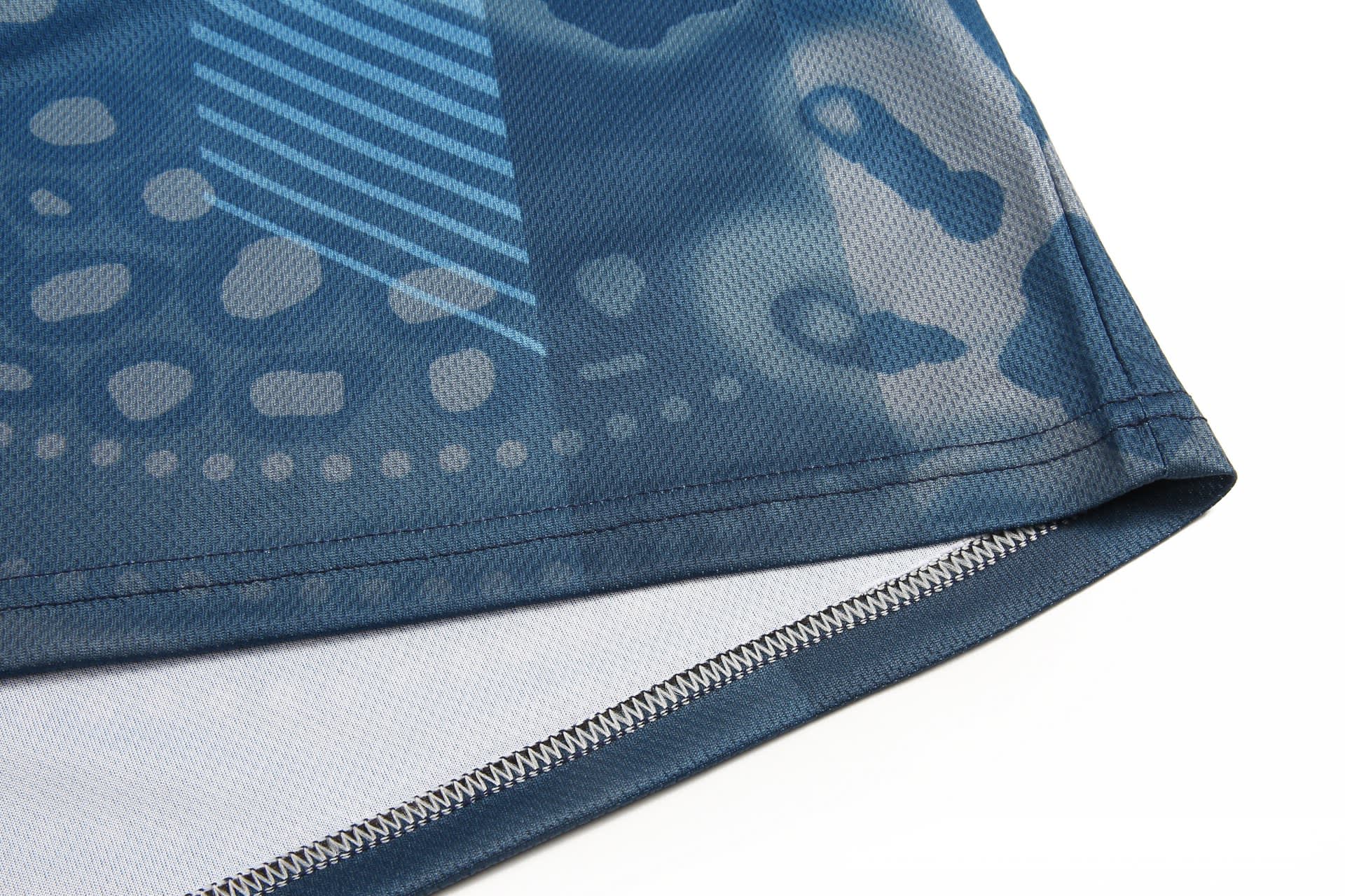 A close-up of a blue and grey sports uniform featuring a textured design and stitched hem. It includes a logo.
