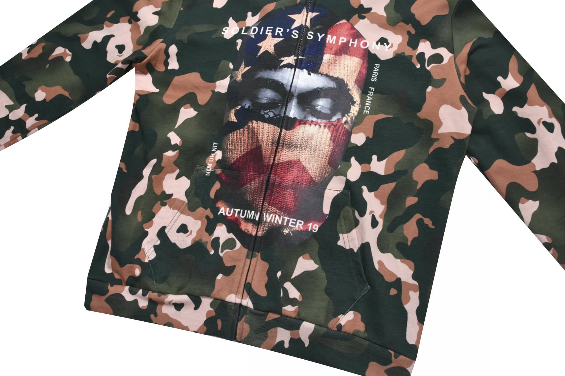 A camouflage-patterned hoodie featuring a direct print graphic of a masked figure against an American flag backdrop.