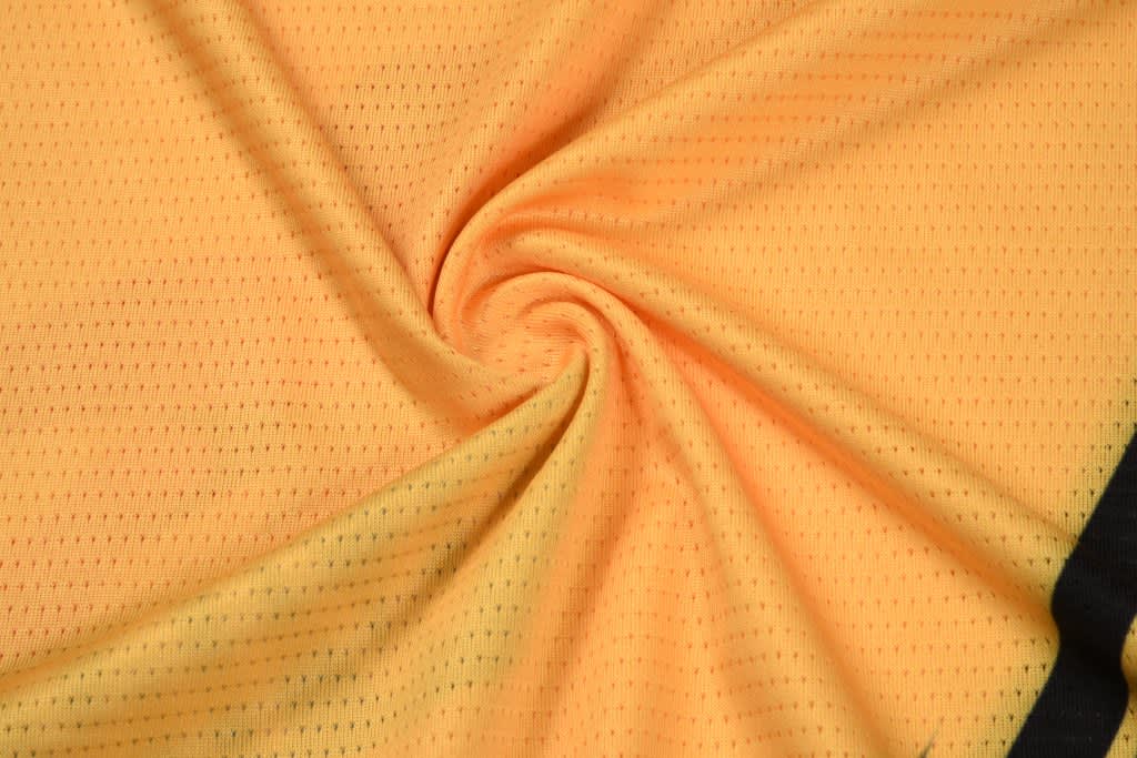 A yellow fabric featuring a textured pattern, arranged in a spiral formation. The fabric has a black section along the edge and includes branding.