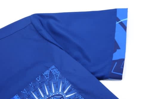 A blue cotton shirt with a detailed graphic design on the sleeve and front. The shirt features a logo.