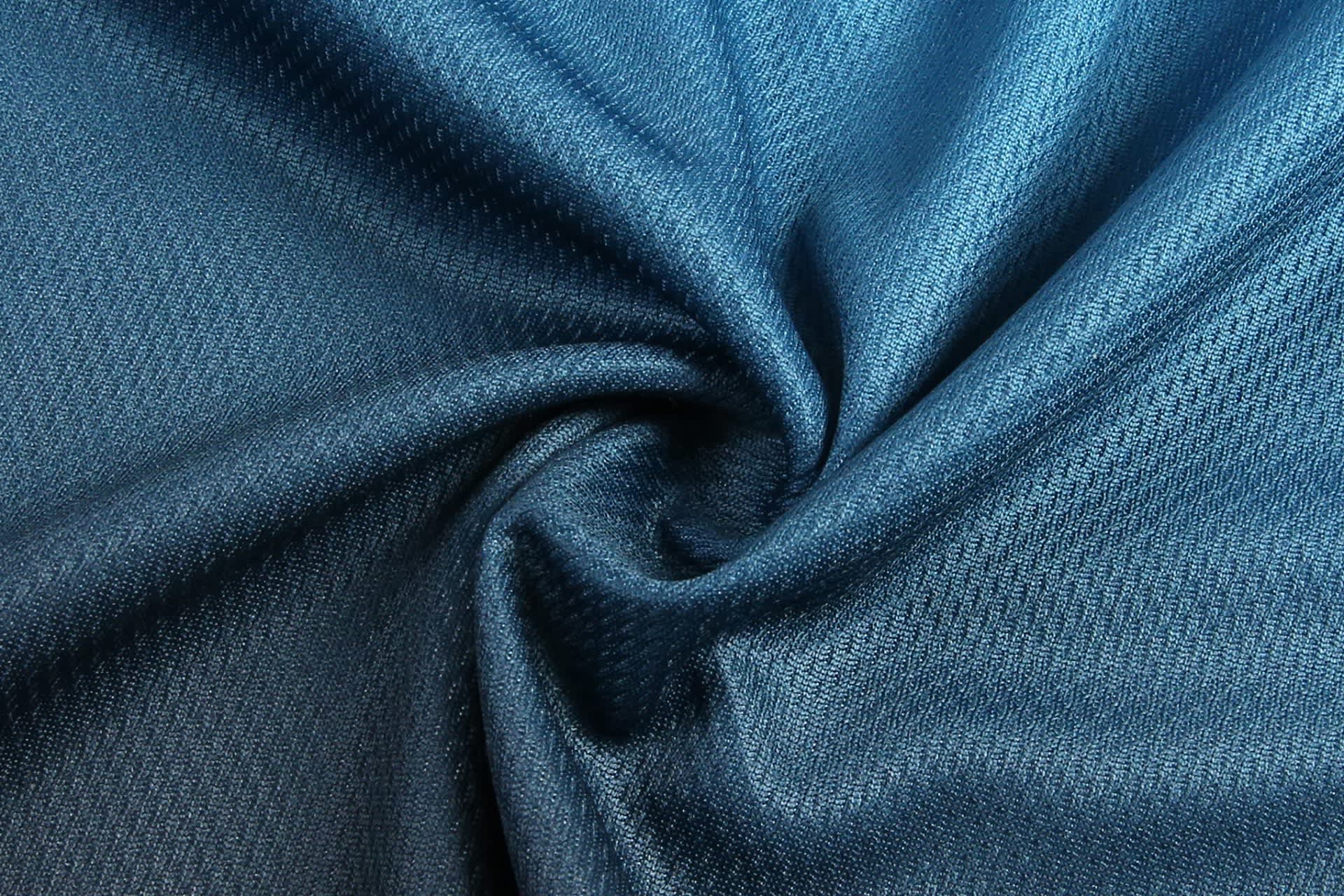 A close-up of dark teal fabric with a textured weave, featuring a spiral pattern.